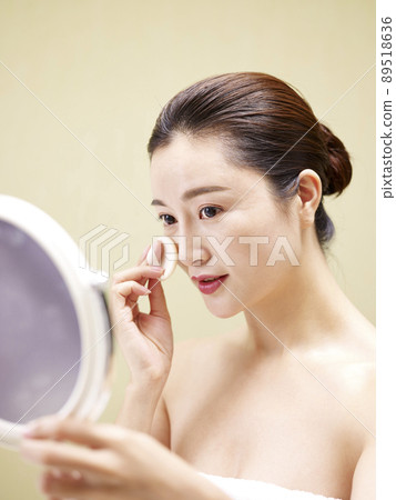 beautiful young asian woman looking in the mirror while cleansing face with a sponge 89518636