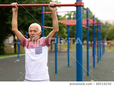 Elderly man hanging from pullup bar and doing pull-ups 89519250