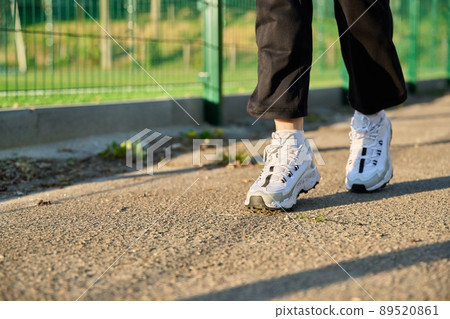 Close-up of female legs in white sneakers running along the road near the stadium Close-up of female legs in white sneakers running along the road near the stadium 89520861