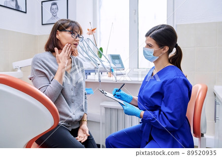 Dental office visit, female patient talking to doctor, dentist making notes 89520935