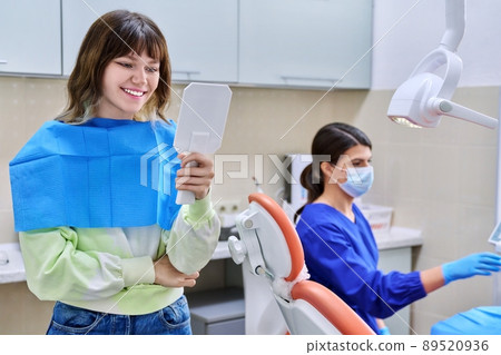 Teenage female looking at healthy teeth in mirror, in dental office 89520936
