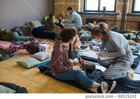 Young clinician checking up throat of little boy sitting next next to his mother 89525241