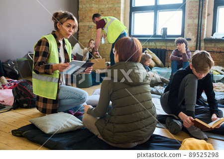 Female volunteer with mobile gadgets communicating to one of refugees 89525298