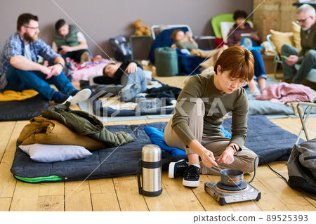 Young hungry Asian female refugee cooking food in small pan on the floor 89525393