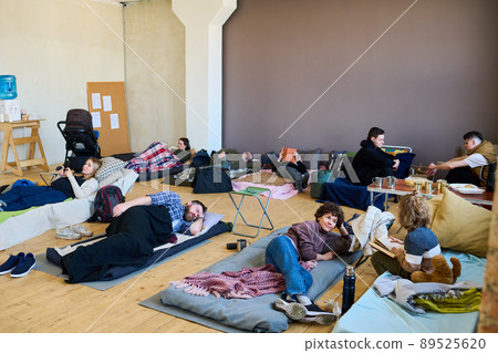 Several refugees having rest on their sleeping places in spacious room Several refugees having rest on their sleeping places in spacious room 89525620
