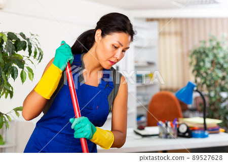 Female room cleaner sweeping floor in modern office Female room cleaner sweeping floor in modern office 89527628