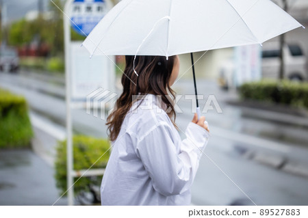 A woman holding an umbrella and waiting at a bus stop bus station A woman holding an umbrella and waiting at a bus stop bus station 89527883