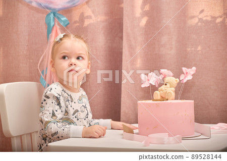 A little girl in pajamas on her birthday sits on a white chair at a children's table, on which there is a birth. 89528144