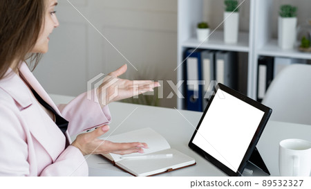Virtual conference. Female speaker. Digital mockup. Unrecognizable woman talking to tablet computer with blank screen gesturing hands in light room interior. Virtual conference. Female speaker. Digital mockup. Unrecognizable woman talking to tablet computer with blank screen gesturing hands in light room interior. 89532327