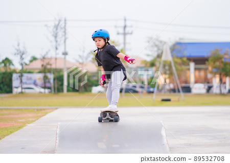 Child or kid girl playing surfskate or skateboard in skating rink or sports park at parking to wearing safety helmet elbow pads wrist and knee support 89532708