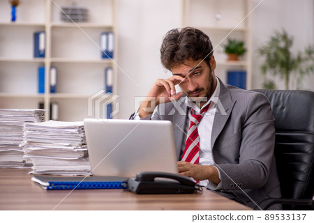 Young male employee unhappy with excessive work in the office Young male employee unhappy with excessive work in the office 89533137