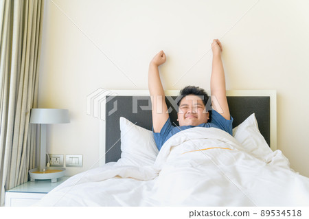 Obese boy wake up and stretch arm on bed in morning. lazy concept Obese boy wake up and stretch arm on bed in morning. lazy concept 89534518