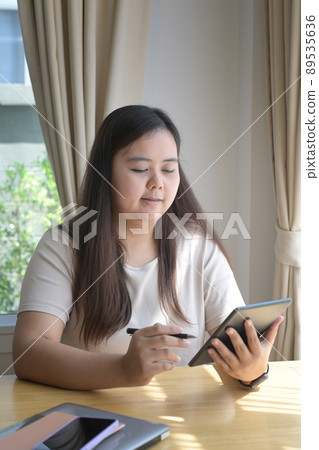 Smiling young woman checking email, social network on digital tablet while sitting in comfortable home. 89535636