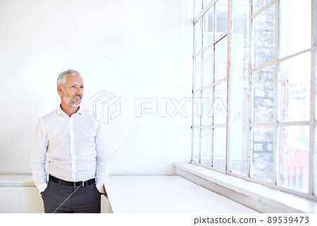 Hes got a vision for his business. A mature businessman looking out a window while standing with his hands in his pockets. 89539473