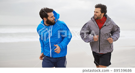 Taking a morning run on the beach. Cropped shot of two young men jogging together along the beach on an overcast morning. 89539686