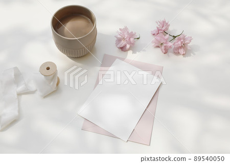 Wedding composition. Feminine spring breakfast still life. Pink Japanese cherry tree, sakura blossoms in sunlight. Blank greeting card, invitation. Cup of coffee. White dappled table background. 89540050
