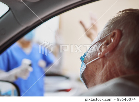 Thank you for the swift service. Shot of a senior man waving at a healthcare worker while in his car at a drive through vaccination site. 89540074