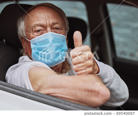 That wasn't so bad. Shot of a senior man showing a thumbs up in his car at a drive through vaccination site. 89540097
