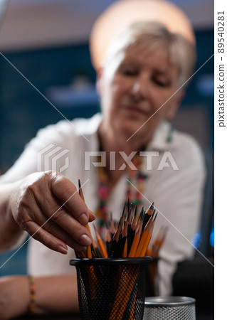 Closeup of elderly sketch artist hand picking graphite hb pencil for drawing still nature in home studio. Creative retired citizen choosing instrument for creating masterpiece in workshop. 89540281