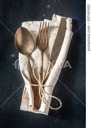 Cutlery. A spoon, a fork, and a knife in a rustic napkin on black 89540992