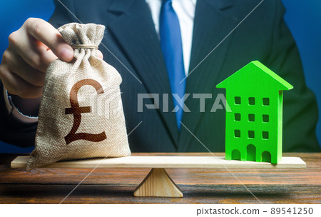 Businessman puts british pound sterling money bag on scales and green house. Investment in renovation. Reduced CO2 emissions, energy efficiency. Profitability housing of eco technologies. Businessman puts british pound sterling money bag on scales and green house. Investment in renovation. Reduced CO2 emissions, energy efficiency. Profitability housing of eco technologies. 89541250