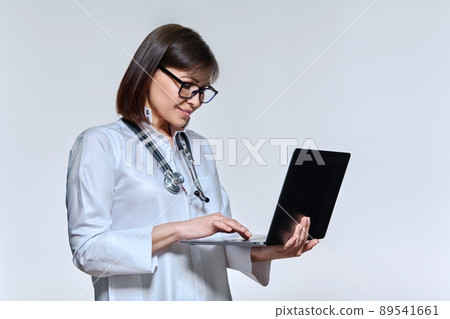 Portrait of female doctor using laptop, on light studio background Portrait of female doctor using laptop, on light studio background 89541661