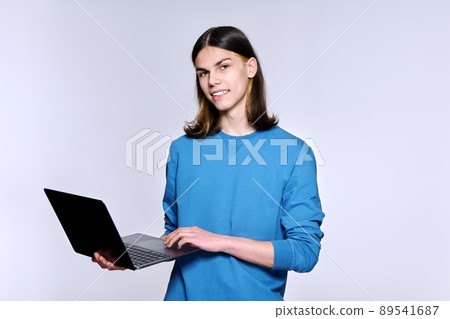 Teenage male student using laptop posing looking at camera on light studio background 89541687