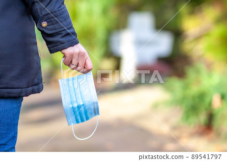 Woman, standing at the grave of family members with a facemask during the pandemic Woman, standing at the grave of family members with a facemask during the pandemic 89541797
