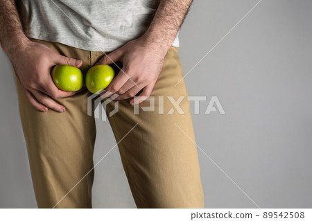 A man in beige jeans at the level of the genitals , holding a ripe and rotten apple. Disease for men. The concept of protection of sexually transmitted infections. Copy space 89542508