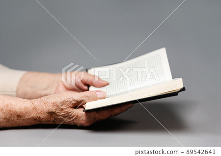 Wrinkled hands of a senior woman are holding a book with sacred religious texts. Gray background. The concept of religion and prayer 89542641