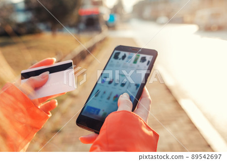 The concept of online shopping. Women's hands hold a smartphone with a blurred screen, and a Bank card, making purchases online in the online store The concept of online shopping. Women's hands hold a smartphone with a blurred screen, and a Bank card, making purchases online in the online store 89542697