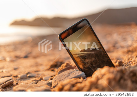 The concept of the photos on the phone. The smartphone lies buried in the sand on the beach, and takes a photo of the beach in the background. Copy space The concept of the photos on the phone. The smartphone lies buried in the sand on the beach, and takes a photo of the beach in the background. Copy space 89542698