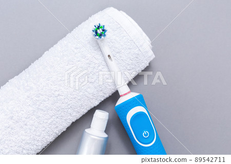Electric toothbrush, toothpaste, and white towel on a gray background. Flat lay. The concept of electronic devices for personal hygiene Electric toothbrush, toothpaste, and white towel on a gray background. Flat lay. The concept of electronic devices for personal hygiene 89542711