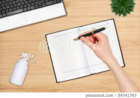 A woman's hand writes with a pen in a notebook. Next to it is a jar with scattered pills. Flat lay. The concept of treatment and planning A woman's hand writes with a pen in a notebook. Next to it is a jar with scattered pills. Flat lay. The concept of treatment and planning 89542763