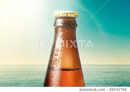 Close-up of the neck of wet glass bottle of dark beer against the background of the ocean and the sky. Alcoholic beverages on vacation Close-up of the neck of wet glass bottle of dark beer against the background of the ocean and the sky. Alcoholic beverages on vacation 89542766