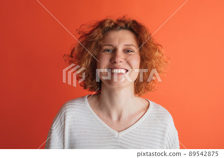 Portrait of beautiful emotive red-haired woman cheerfully smiling, posing isolated over red studio background 89542875