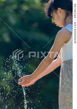 A cute elementary school girl washing her hands in a park in the middle of summer 89546188