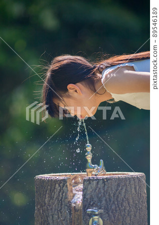 一個可愛的小學女孩在仲夏時在公園裡喝自來水 一個可愛的小學女孩在仲夏時在公園裡喝自來水 89546189
