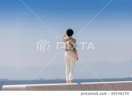 Back view of a young woman taking a walk on the embankment of the summer coast Back view of a young woman taking a walk on the embankment of the summer coast 89546259