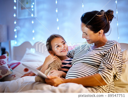You picked a good one. Cropped shot of an attractive young pregnant woman reading her daughter a bedtime story on a tablet. 89547751