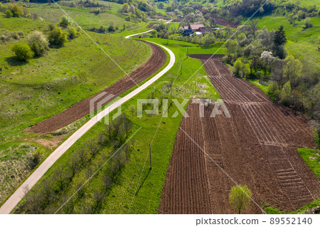 Aerial view of village road passing near an agricultural field Aerial view of village road passing near an agricultural field 89552140