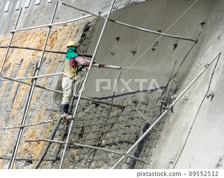 SELANGOR, MALAYSIA -MARCH 4: Construction workers are spraying liquid concrete onto the slope surface to form a retaining wall layer. It acts to prevent erosion on the slope surface. 89552512