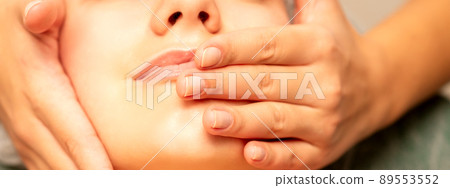 Beautiful young caucasian woman with closed eyes receiving a facial massage in a beauty salon Beautiful young caucasian woman with closed eyes receiving a facial massage in a beauty salon 89553552
