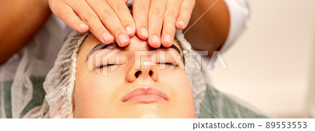 Head massage. Beautiful caucasian young white woman receiving a head and forehead massage with closed eyes in a spa salon Head massage. Beautiful caucasian young white woman receiving a head and forehead massage with closed eyes in a spa salon 89553553