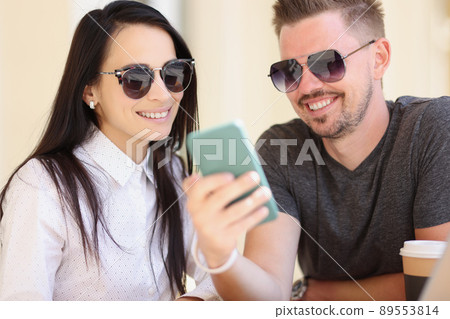 Couple watch memorable pictures on smartphone, go through pics from holiday Couple watch memorable pictures on smartphone, go through pics from holiday 89553814