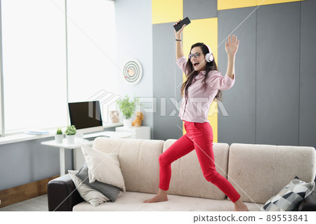 Happy woman dancing on couch, listen to music in headset and sing 89553841