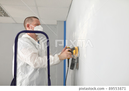 Male worker in protective costume polish wall with special equipment 89553871