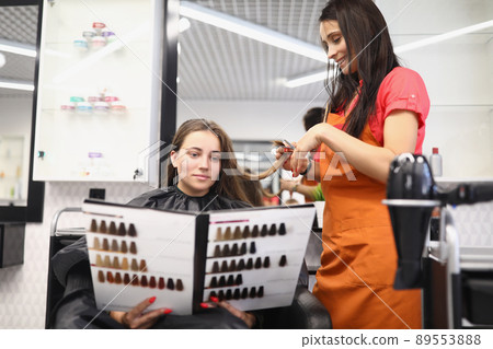 Client look in folder with hair colour samples, hairdresser work on hairstyle 89553888