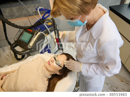 Top view of a young woman receiving facial laser beauty treatment for removing age and pigments spots on her face. Anti-aging procedures. 89553983