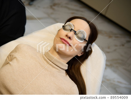 Top view of a young pretty woman wearing UV protective goggles and lying down on the daybed in a wellness spa clinic 89554009